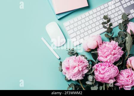 White computer keyboard, mouse, peony flowers, eucalyptus flowers on blue background. Top view. Copy space. Flat lay. Feminine workspace. Blogger Stock Photo