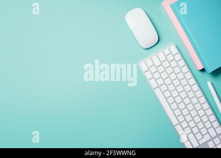Home designer office workspace. White mouse, keyboard, notebook, pen on blue background. Top view. Copy space. Flat lay. Remote job, work. Feminine Stock Photo