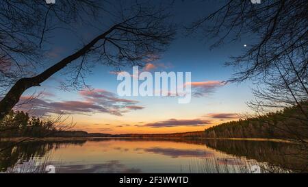 Epic red sunset sky above the lake and forest. Dramatic cloudscape. Symmetry reflections on the water, natural mirror Stock Photo