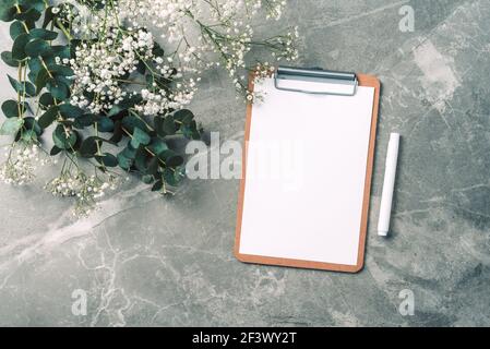 Paper blank, clipboard, pen, eucalyptus branches, gypsophila flowers on marble background. Flat lay, top view. Copy space. Blogger, feminine business Stock Photo