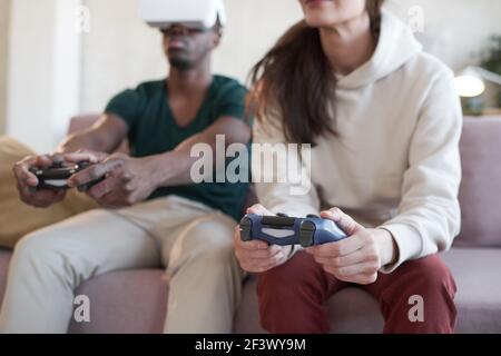 Young couple using joysticks and playing video game together on sofa in the room Stock Photo