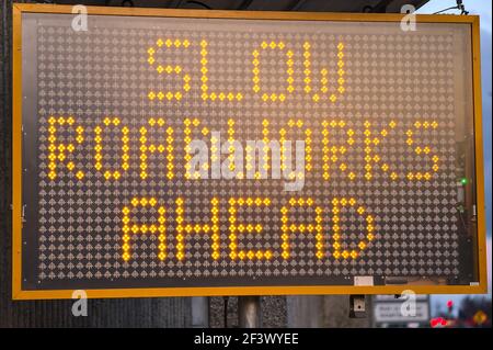 LED traffic control road sign solar powered message board mobile trailer variable message signs displaying Slow Roadworks Ahead along motorway, Dublin Stock Photo
