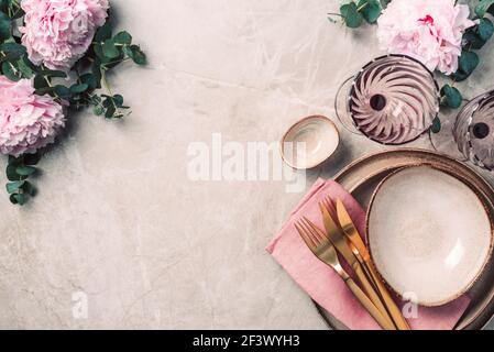 Tableware, flowers for serving a festive table, dinner. Stoneware plates, golden cutlery, eucalyptus branches, peony flowers on marble background Stock Photo