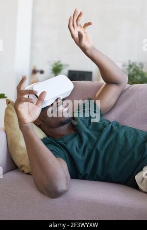 African man wearing vr glasses lying on sofa and gesturing during game Stock Photo