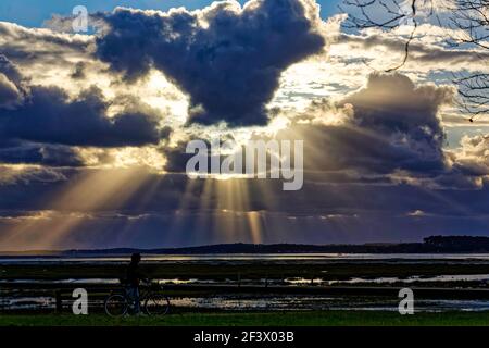 Ares (south-western France): sunset over the Arcachon Bay in autumn. Rays of sun through clouds, rays of light and silhouette of someone riding a bike Stock Photo