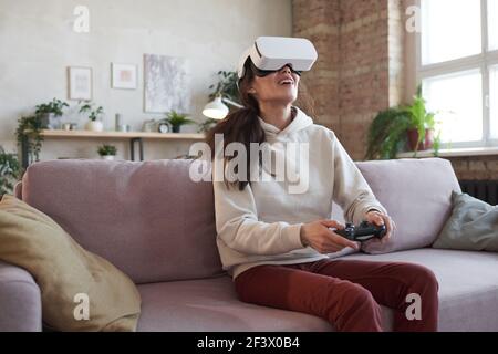 Young woman in vr glasses sitting on sofa and using joystick during her video game Stock Photo