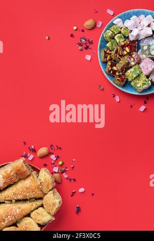 Middle Eastern sweets on red background. Arab dessert, baklava, halva, rahat lokum, sherbet, nuts, pistachios, dates, raisins, dried apricots Stock Photo