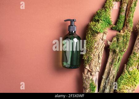 Green glass bottle of shampoo, soap, conditioner on brown background with natural moss over bark, wood. Top view, copy space. Blank label for mock-up Stock Photo