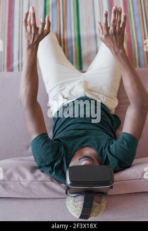 Excited young man in virtual reality headset playing video game at home, trying to entertain himself at home Stock Photo
