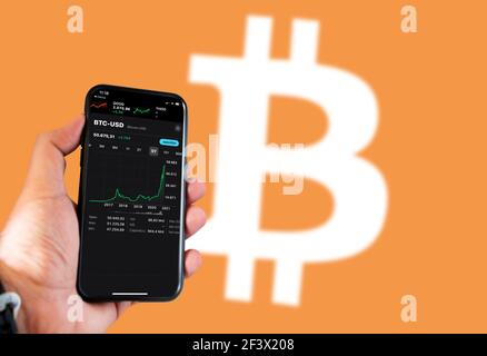 Rome, Italy, February 2021: Variations in the value of the Bitcoin cryptocurrency against the dollar on a phone screen with the Bitcoin logo blurred o Stock Photo