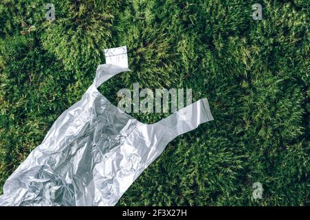 Pollution problem concept. Disposable plastic bag on green moss, grass background. Top view. Copy space. Environmental pollution problem. Garbage Stock Photo