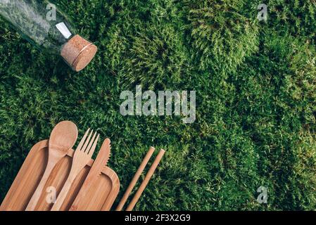 Glass bottle, eco-friendly bamboo cutlery, packaging, containers for takeaway food for picnic or lunch on green moss background. Top view. Copy space Stock Photo