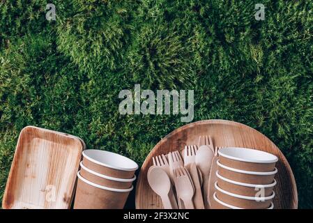 Disposable tableware from natural materials. Bamboo plates, wooden spoon, fork, knife, paper cups on green moss background. Eco-friendly sustainable Stock Photo