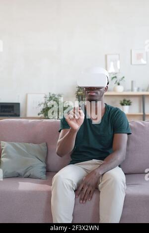 African man sitting on sofa and using VR goggles at home Stock Photo