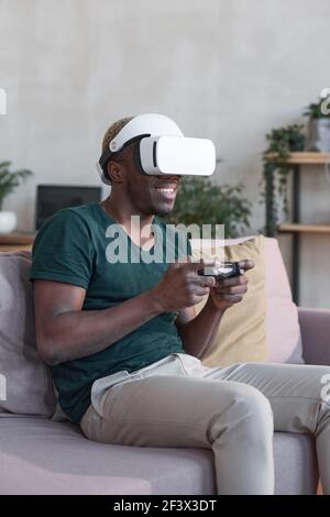 African young man with virtual reality headset and joysticks playing video games home Stock Photo