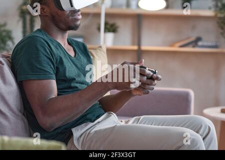 African man in vr glasses using joystick to play video game on sofa at home Stock Photo