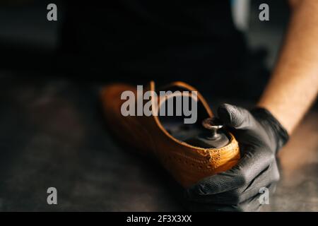 Close-up hands of shoemaker shoemaker wearing black gloves inserts wooden shoe block into worn light brown leather shoes Stock Photo