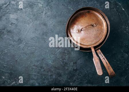 Old vintage copper pots on dark background. Kitchen utensils. Rustic pan. Top view, copy space for your text Stock Photo