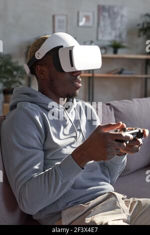 African man in glasses sitting on sofa and using joystick he playing video game at home Stock Photo