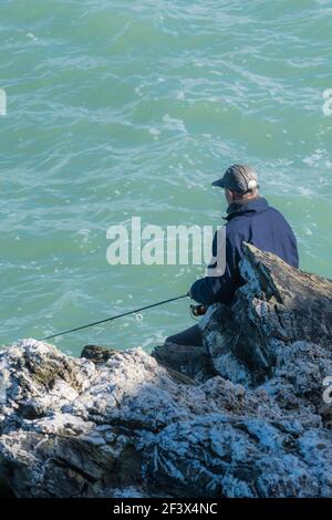 A mature man fishing from rocks at Towan Head in Newquay in Cornwall. Stock Photo
