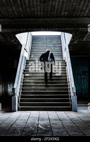 Man dressed in black with crossbody bag runs up the stairs away from the dirty passage Stock Photo