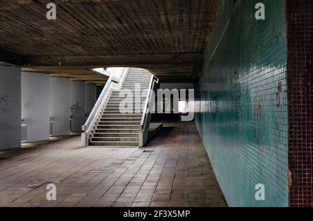 Old urban subway with empty stairway, concrete ceiling, worn brown tiles on the floor and green mosaic on the wall Stock Photo