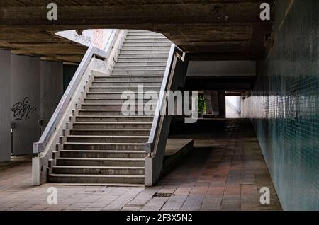 Old urban passage with empty stairway, concrete ceiling, worn brown tiles on the floor and green mosaic on the wall Stock Photo