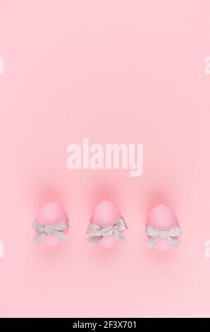 Elegant easter eggs with silver bows in row on pastel pink background, vertical, stories. Stock Photo