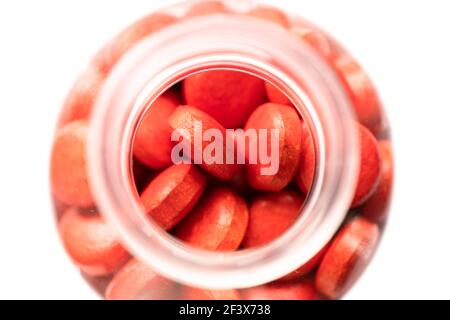 Glass or plastic bottle with a narrow neck, filled with red pills and tablets isolated on white background. Close-up view from above, focus on the top Stock Photo