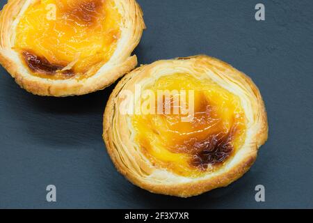 Two small custard tarts on a dark grey background. Stock Photo