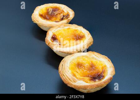 Three small custard tarts on a dark grey background. Stock Photo