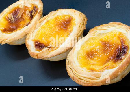 Three small custard tarts on a dark grey background. Stock Photo