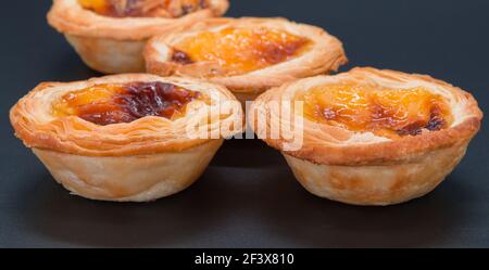 Four small custard tarts on a dark grey background. selective focus on the front two tarts and softens through the view of the image. Stock Photo
