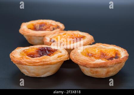 Four small custard tarts on a dark grey background. selective focus on the front two tarts and softens through the view of the image. Stock Photo