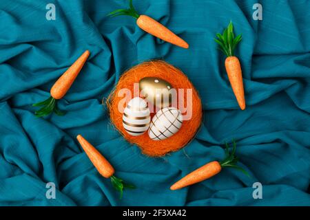 Minimal layout of golden Easter eggs  in orange nest with bunny carrot circling around against cyan or blue background. Stock Photo