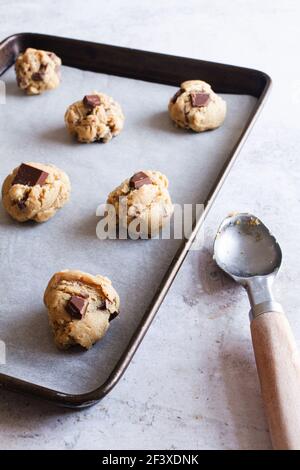 Raw chocolate chip cookie dough on a baking tray with ice cream scooper to the side. Stock Photo