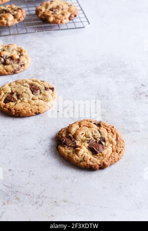 Freshly baked chocolate chip and hazelnut cookies with a few cooling on a wire rack in the background. Stock Photo