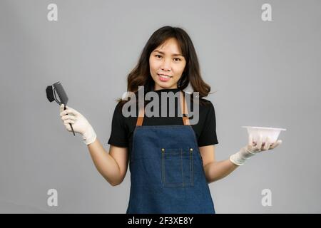 Portrait of Asian gorgeous cheerful young female professional hairdresser holding applied hair color with a brush smiling to the camera posing at her Stock Photo