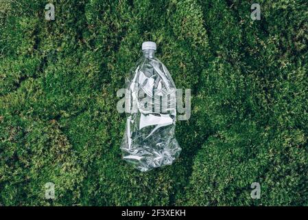 Empty rumpled used plastic bottle on green moss, grass background. Top view, copy space. Pollution, environmental protection concept. Reuse garbage Stock Photo