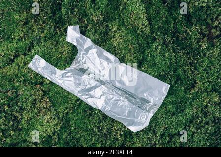 Pollution problem concept. Disposable plastic bag on green moss, grass background. Top view. Copy space. Environmental pollution problem. Garbage Stock Photo