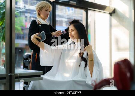 Image of a happy positive young beautiful woman client take a selfie with hair stylist in hair salon. Stock Photo