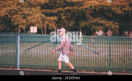 An elderly man wearing a facemask walking on the walkway on the street Stock Photo