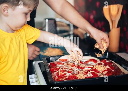 Father and son sprinkle grated cheese on pizza. Preparing for the