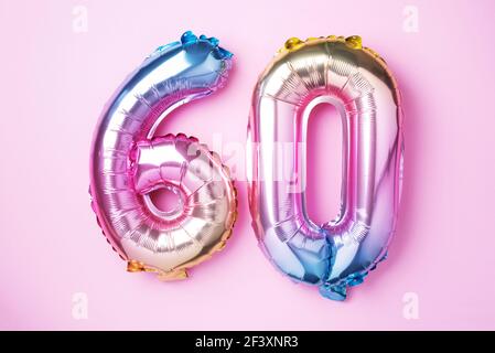 Rainbow foil balloon number, digit sixty. Birthday greeting card with inscription 60. Anniversary concept. Top view. Colored numeral on pink Stock Photo