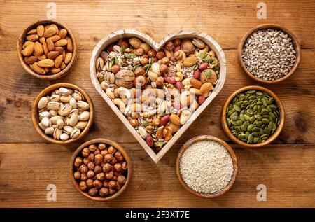 Heart shaped box and small bowls full of nuts and seed on rustic table. Stock Photo