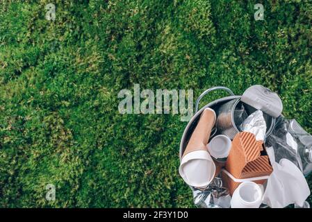 Plastic waste, food packaging in trash bin trash collection on green moss background after picnic in forest. Plastic free. Top view. Recycling plastic Stock Photo