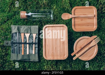 Glass jar, bottle, metal cup, straws for drinking, bamboo cutlery and lunch boxes on green grass, moss background. Top view. Sustainable lifestyle Stock Photo