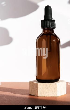Amber cosmetic bottle on wooden geometric pedestal podium, product packaging with natural shadows from plants, anti aging serum, cosmetics mockup Stock Photo