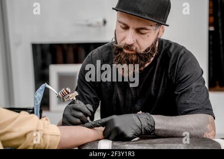 Male tattoo master tattooing female client. Tattoo machine and lamp. Workplace artist. Creating picture on hand with it in salon. Stock Photo