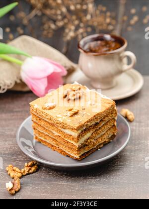 Slice of layered honey cake on a plate with cup of coffee and tulip flower, selective focus Stock Photo